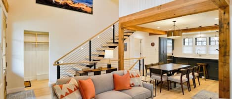 Un vaste espace de vie comprenant un canapé gris, une table à manger en bois et un escalier menant aux étages supérieurs.