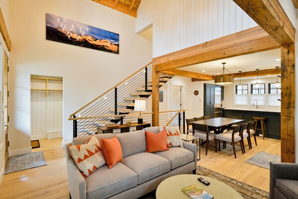 A spacious living area with a gray sofa, wooden dining table, and a staircase leading to upper floors.