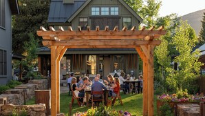 A wooden pergola with a group of people dining at an outdoor table. - Academy Place | King's Crown (Crested Butte)