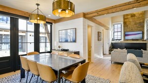 A spacious living area with a large dining table, comfortable seating, a fireplace, and a television. - Academy Place | King's Crown (Crested Butte)