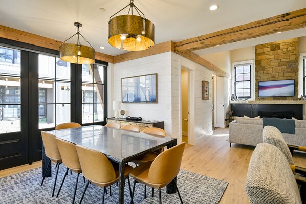 A spacious living area with a large dining table, comfortable seating, a fireplace, and a television.