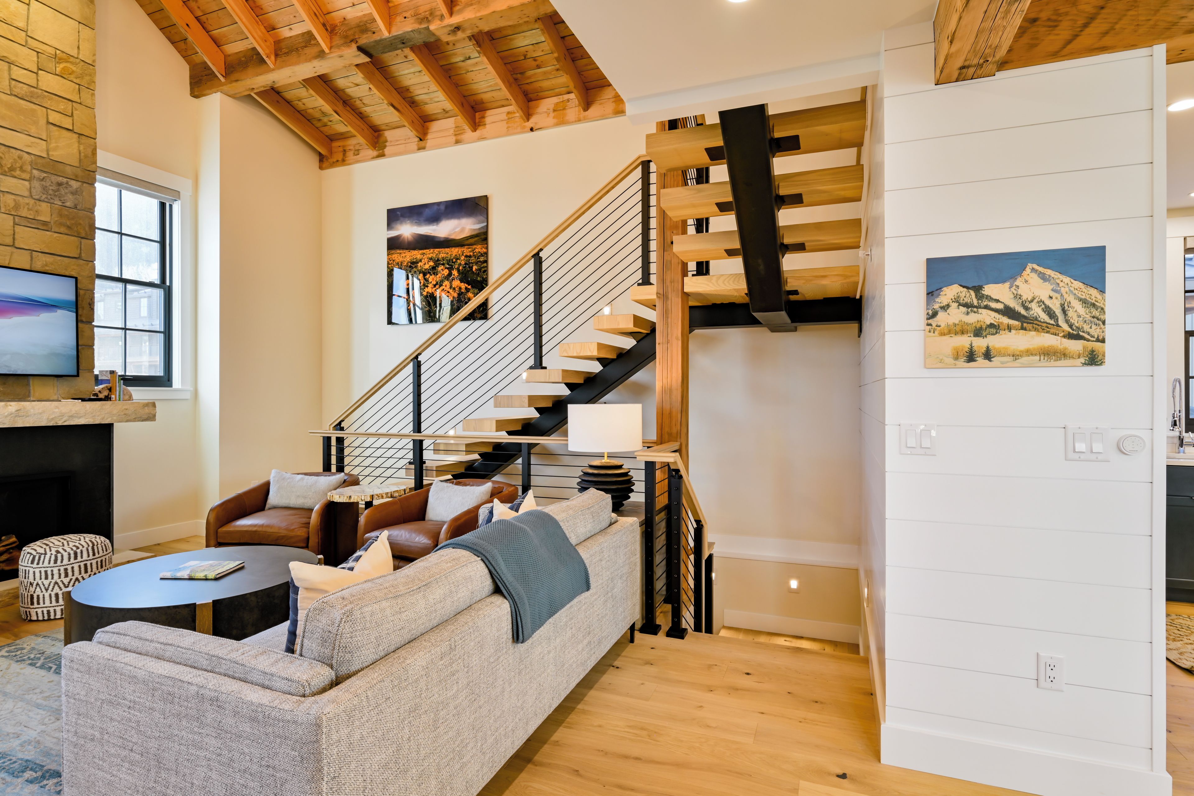 A modern living room with a wooden staircase, leather sofas, and a fireplace.