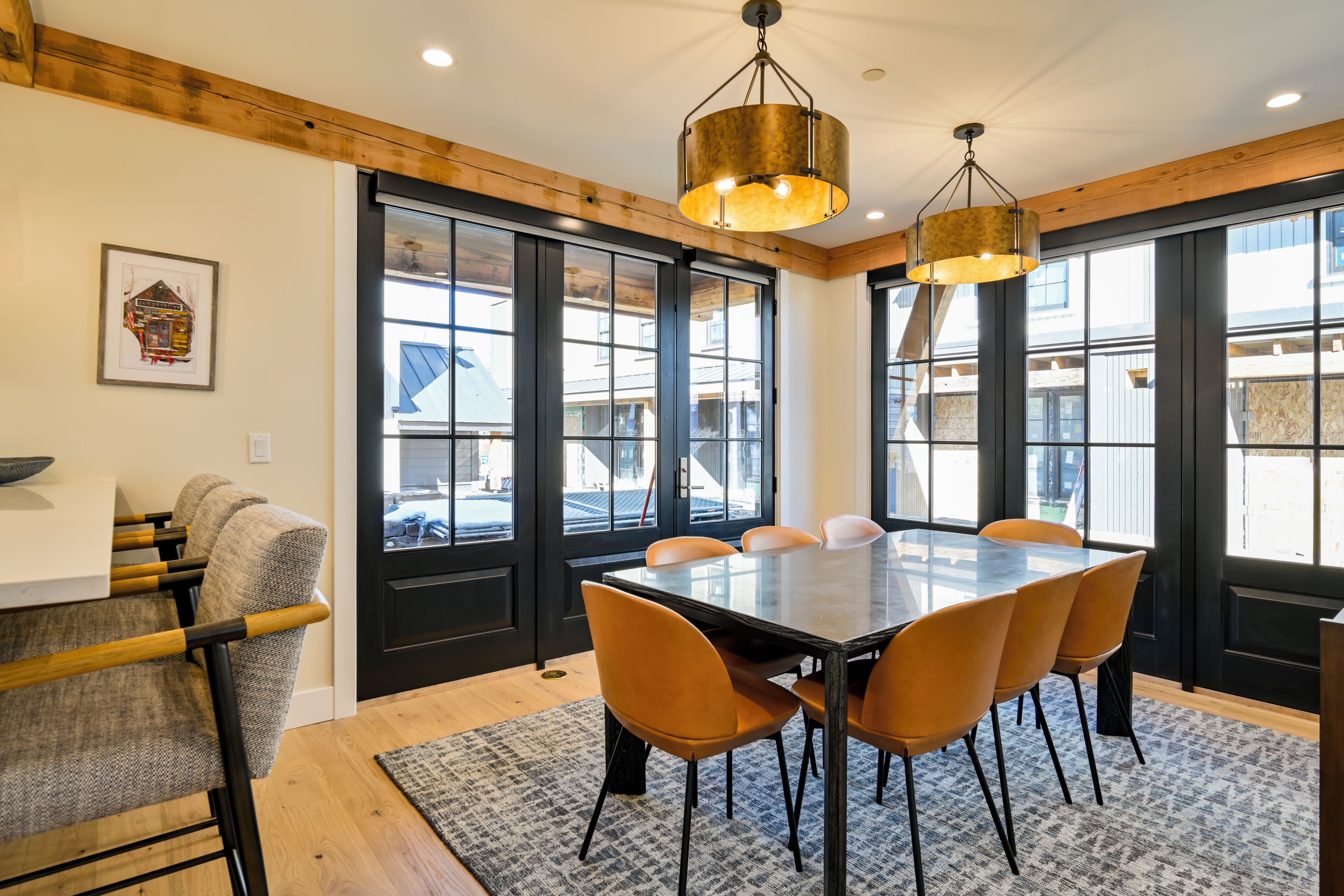 A dining area with a large table and six chairs, a chandelier, and large windows.