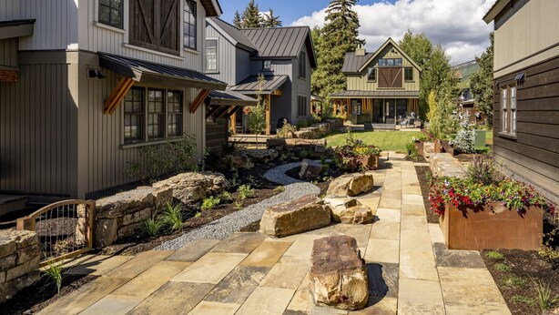 A residential area with stone pathways, a small water feature, and a variety of plants. - Academy Place | King's Crown (Crested Butte)