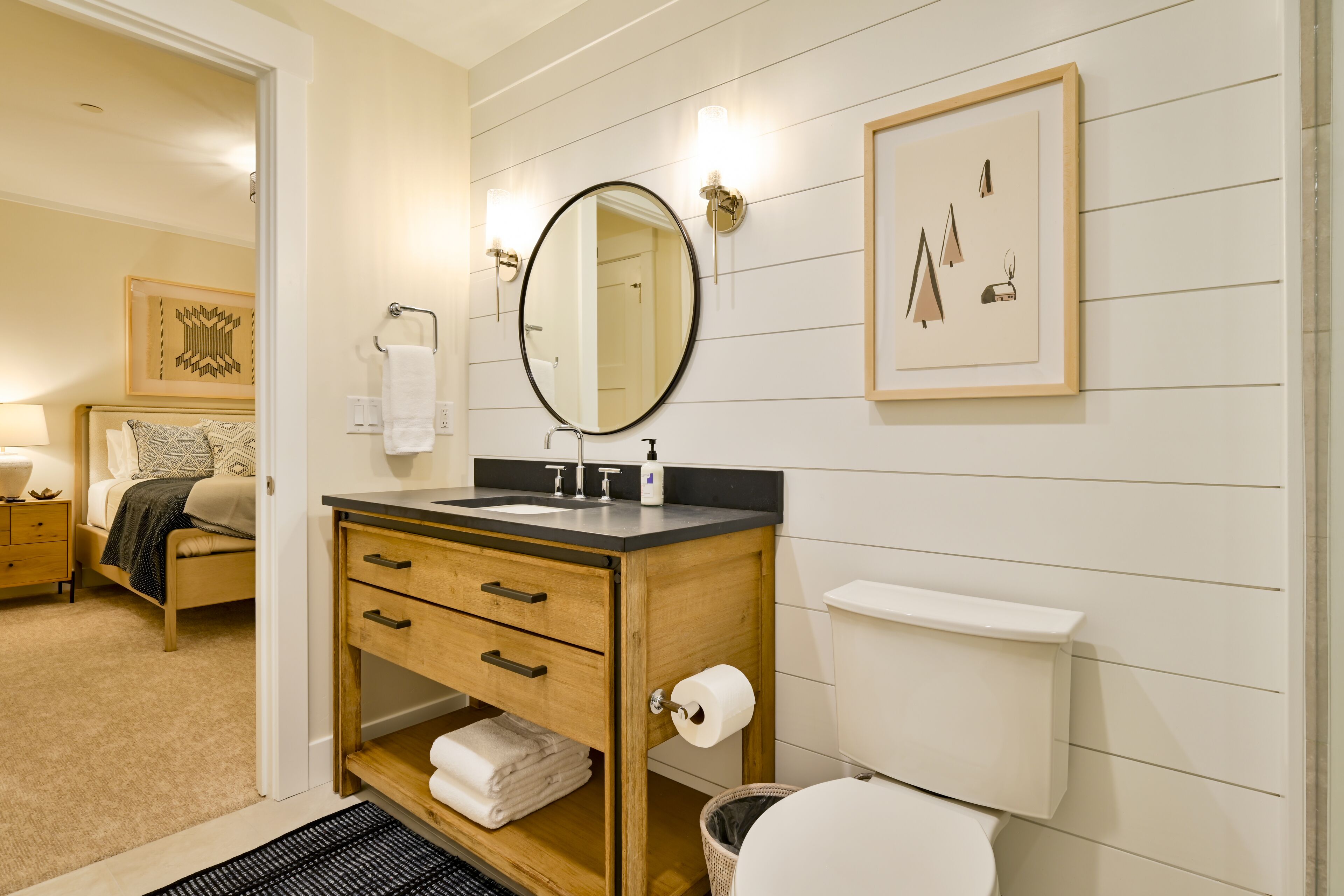 Ein modernes Badezimmer mit einem Holzlagerfläschchen, einem runden Spiegel und einer Toilette.