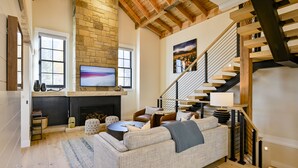 A living room with a fireplace, a staircase, and a large TV mounted on the wall. - Academy Place | King's Crown (Crested Butte)