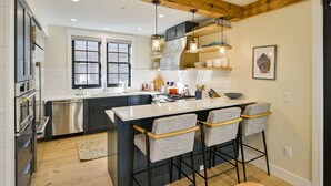 Cocina moderna con una isla central, taburetes de bar, electrodomésticos de acero inoxidable y techo de madera.