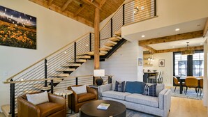 A spacious living area with a staircase, a sofa, a coffee table, and a dining area. - Academy Place | King's Crown (Crested Butte)
