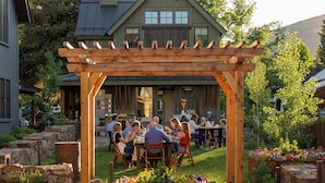 Una pérgola de madera con un grupo de personas cenando en una mesa al aire libre.