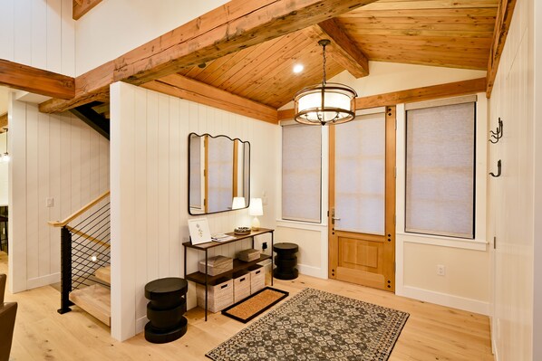 A wooden staircase with a black railing, a console table with a mirror, a patterned rug, and a wooden door with frosted glass panels. - Academy Place | Bluebell (Crested Butte)