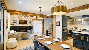 A modern kitchen with stainless steel appliances, wooden beams, and a dining area with a wooden table set for six. - Academy Place | Fairy Slipper (Crested Butte)
