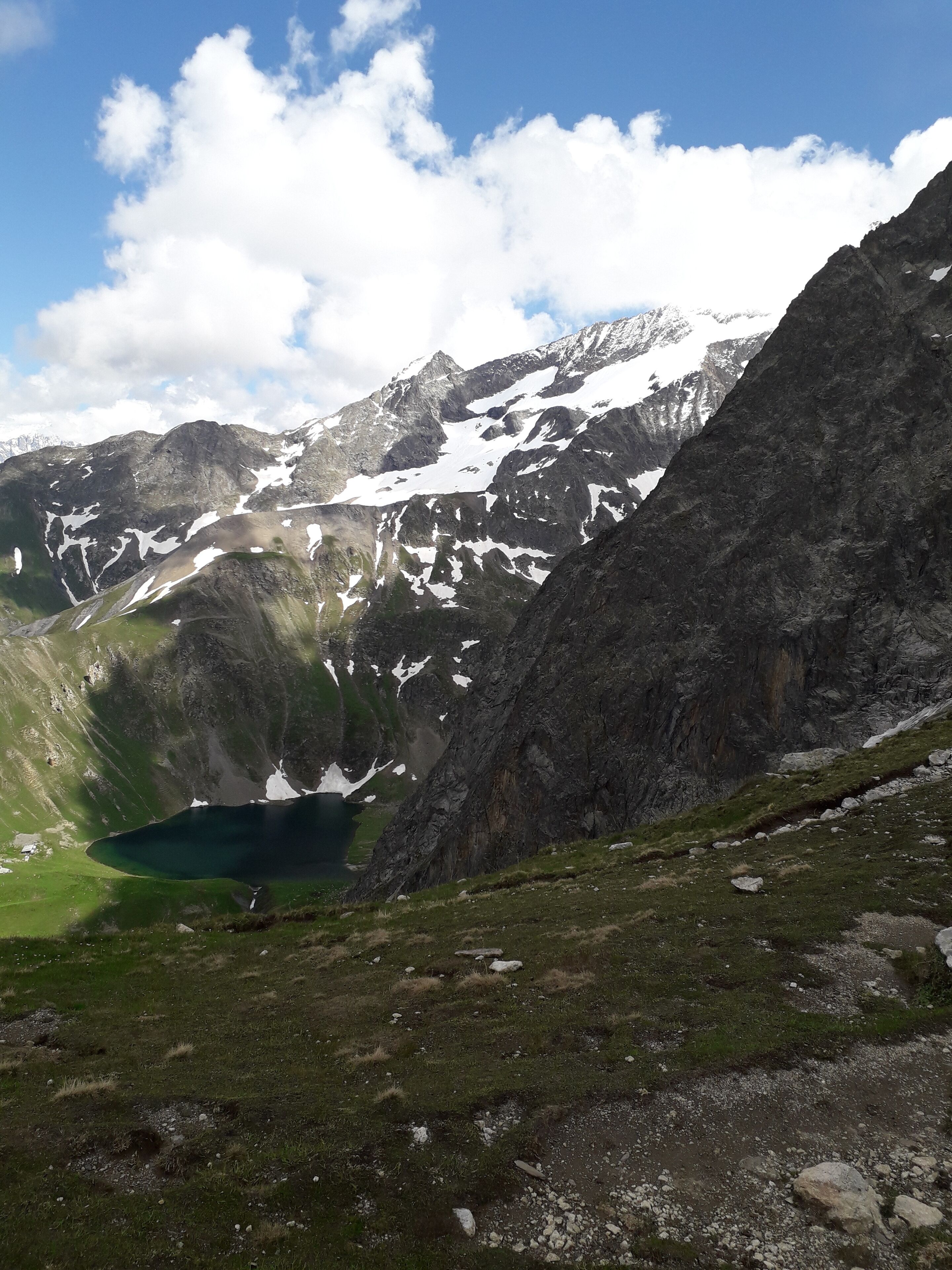 Paesaggio montuoso con un lago, terreno roccioso e chiazze di neve.