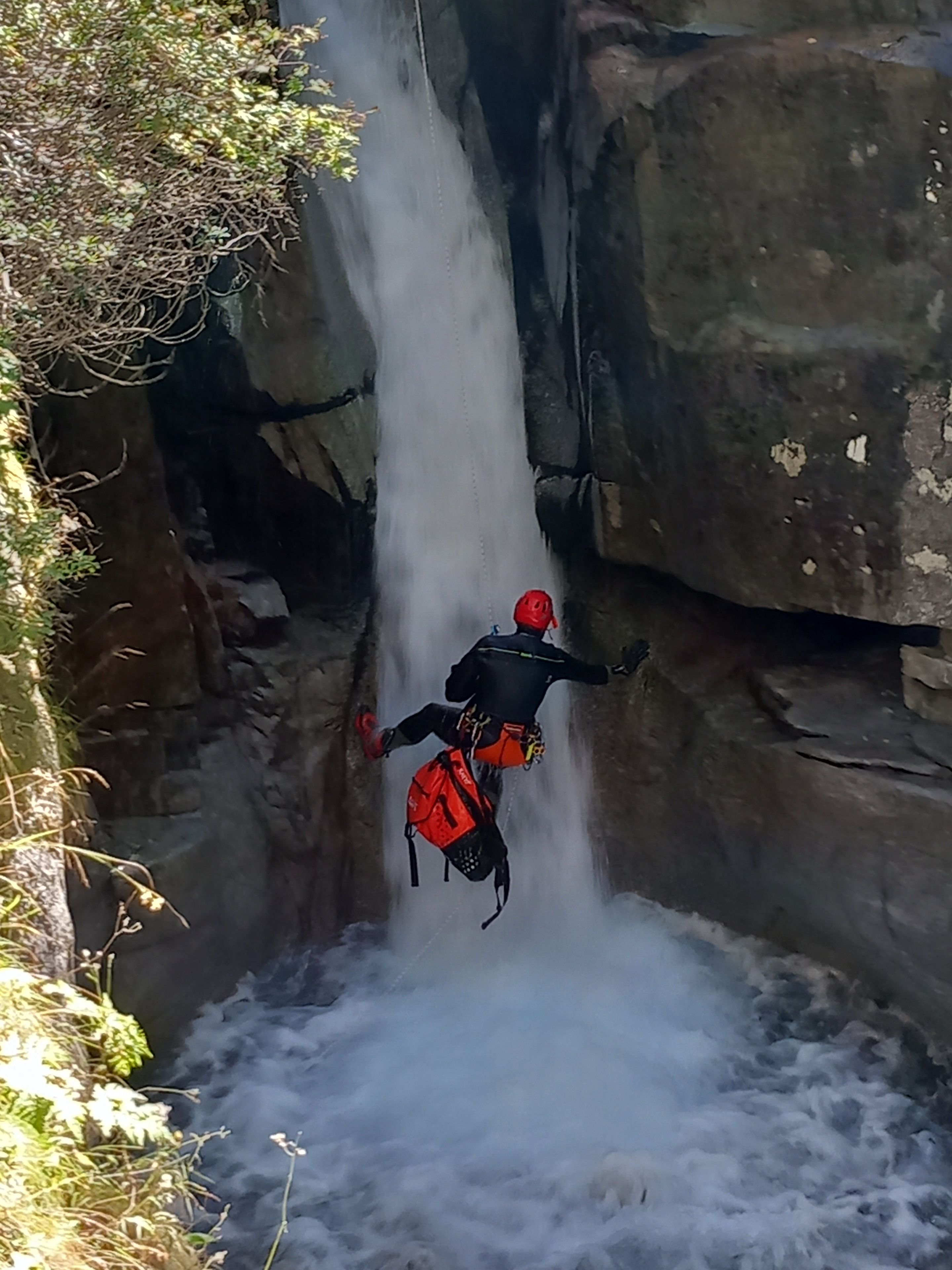 Una persona descendiendo por una cascada con casco y arnés rojos.