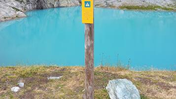 Un cartel de madera con indicaciones y un símbolo de advertencia, sobre un telón de fondo de una montaña rocosa y un lago turquesa.