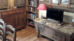 A rustic room with wooden walls, a bookshelf, a desk with a television, and a hanging light fixture.