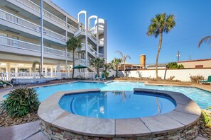 Een hotel met een zwembad, inclusief een jacuzzi, ligbedden en palmbomen.