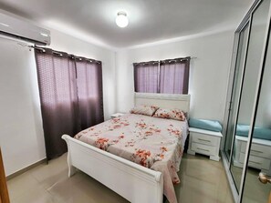 Une chambre à coucher comprenant un lit, une table de chevet, une armoire et un ventilateur de plafond.