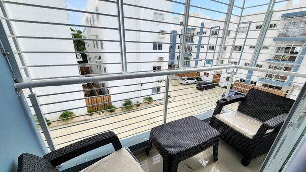 A balcony with wicker furniture, a clear view of the street, and modern buildings in the background.
