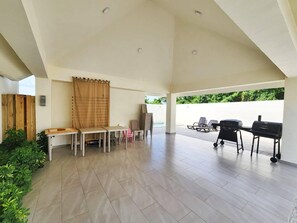 Un patio couvert avec une piscine, des sièges d’extérieur et un espace barbecue.