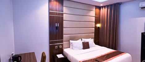 A modern hotel room with a large bed, a desk with a coffee maker, and a built-in wardrobe.