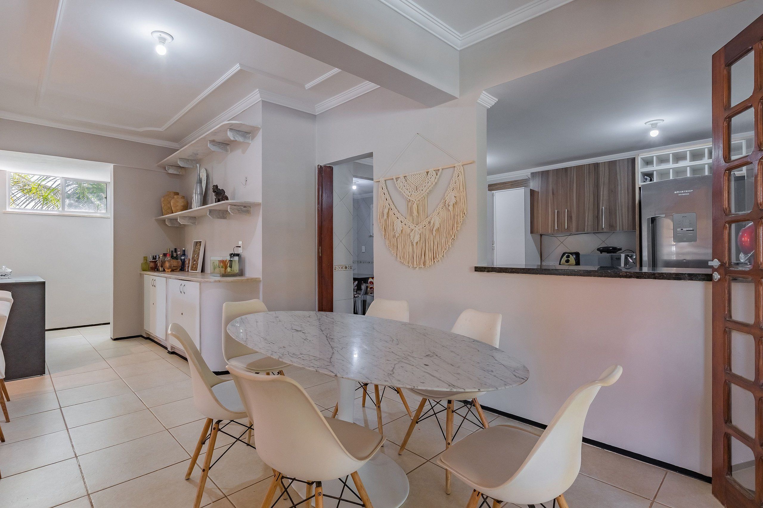 Una cocina moderna con una isla de mármol, sillas blancas y una decoración de macramé colgante.