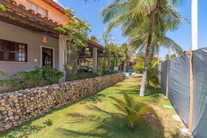 A courtyard with a stone wall, palm trees, and a covered area with a tiled roof.