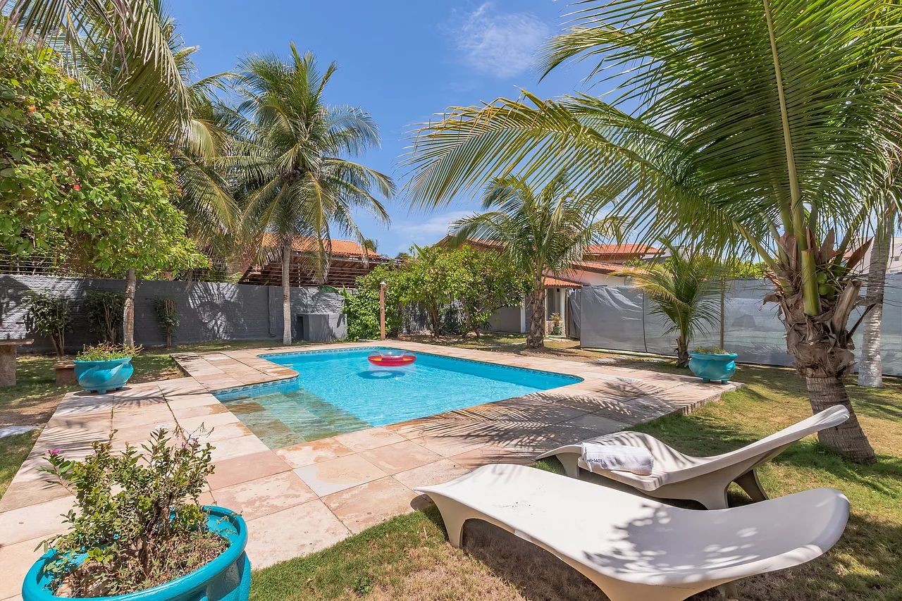 A backyard with a swimming pool, palm trees, and lounge chairs.