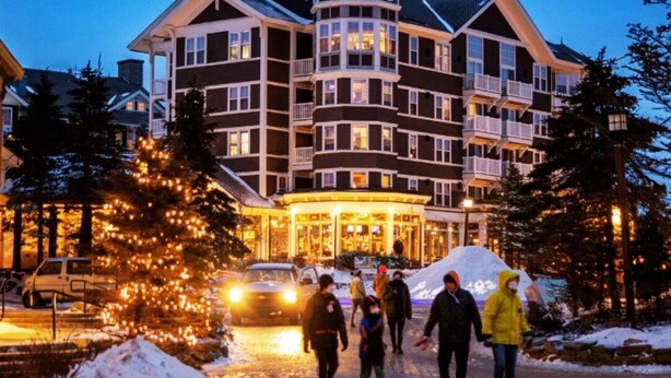 Ein mehrstöckiges Hotel mit einem markanten Glockenturm, einem überdachten Eingang und einer verschneiten Auffahrt.
