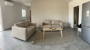 Una sala de estar moderna con un sofá color beige, un sillón a juego, una mesa de centro y un ventanal grande.