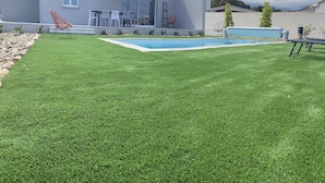 Una casa moderna con piscina, un patio con mobiliario exterior y un césped bien cuidado.