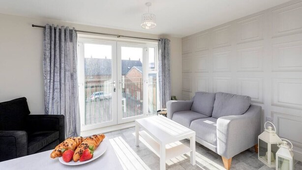 Un salon moderne avec un canapé gris, une table basse blanche et un balcon agrémenté de rideaux.