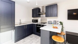 Une cuisine moderne avec des meubles de couleur sombre, un four à micro-ondes, une cuisinière et un évier. On y trouve un petit îlot avec des tabourets et une plante.