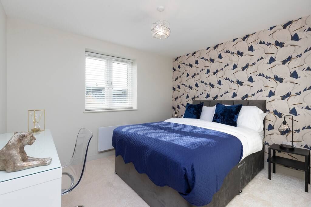 Une chambre à coucher comprenant un lit, une table de chevet, une chaise, une fenêtre et un mur orné d’un motif de feuilles.
