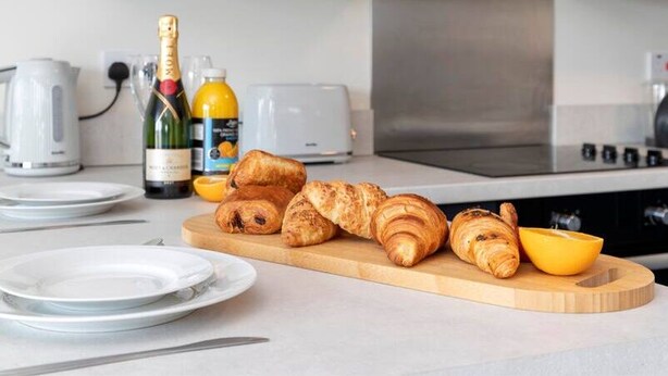 A kitchen counter with croissants, a bottle of champagne, and a toaster. - Avery House - 1 Bed with Outdoor Terrace (Darlington)