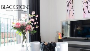 A modern living room with a large flat-screen TV, a vase with flowers, and two white mugs on a table. - Avery House - 1 Bed with Outdoor Terrace (Darlington)