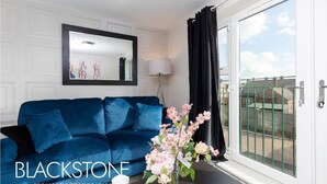 A blue sofa, a mirror, a vase with flowers, and a view through a glass door. - Avery House - 1 Bed with Outdoor Terrace (Darlington)
