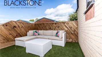 Un jardin avec un canapé d’angle blanc, une table basse blanche et une clôture en bois.