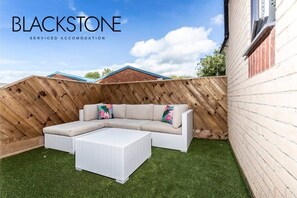 A backyard with a white sectional sofa, a white coffee table, and a wooden fence.