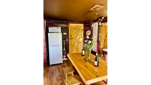 A rustic kitchen with wooden walls, a white refrigerator, a wooden table with a vase of flowers, and a wooden door.