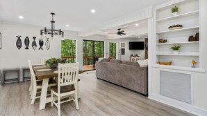 Un salon moderne comprenant un coin repas, un canapé gris, un lustre et un téléviseur fixé au mur.