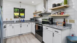 Une cuisine moderne avec des meubles blancs, des plans de travail en granit, une cuisinière en acier inoxydable et un coin café.