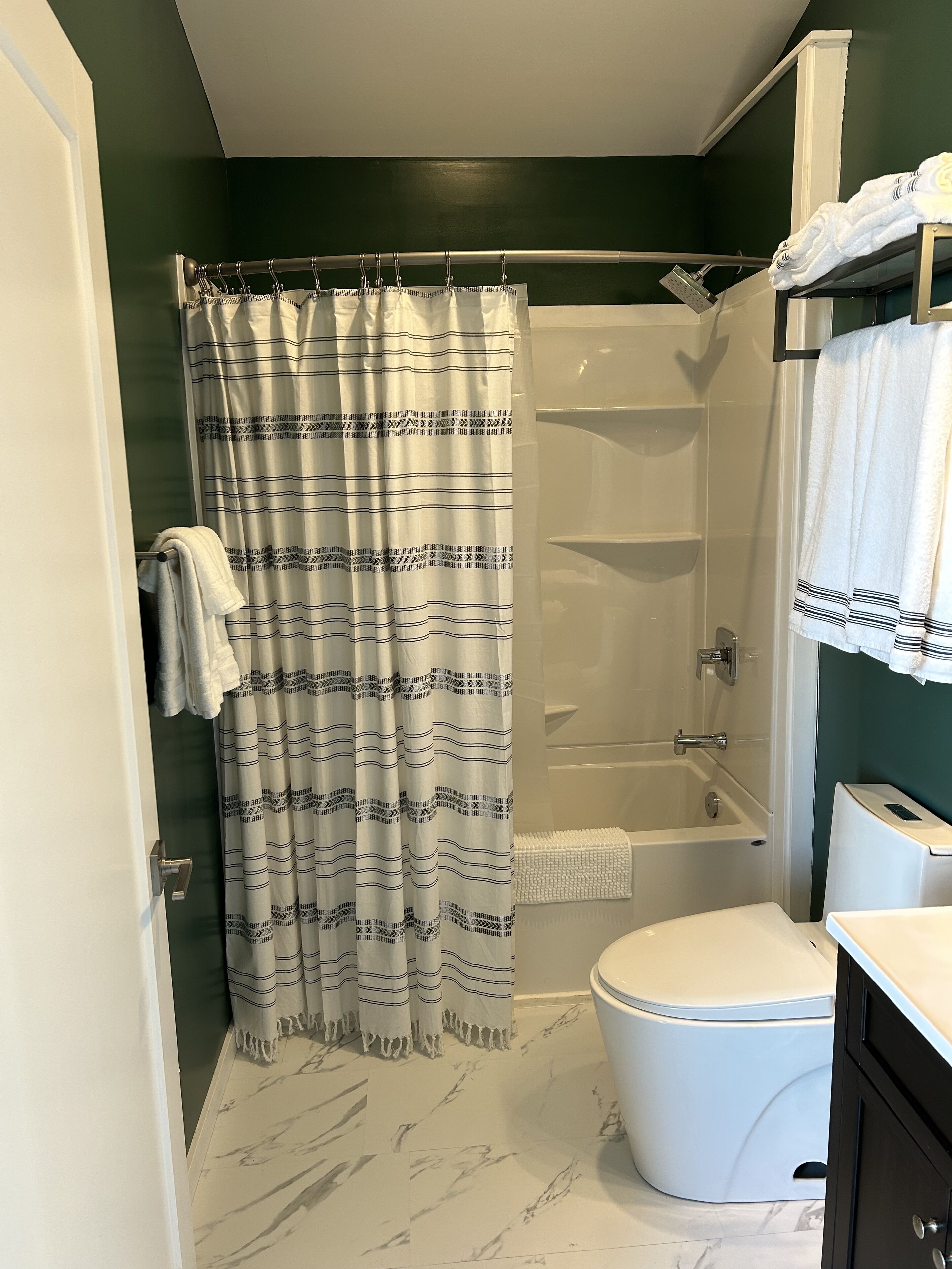 A bathroom with a shower, toilet, and marble flooring.