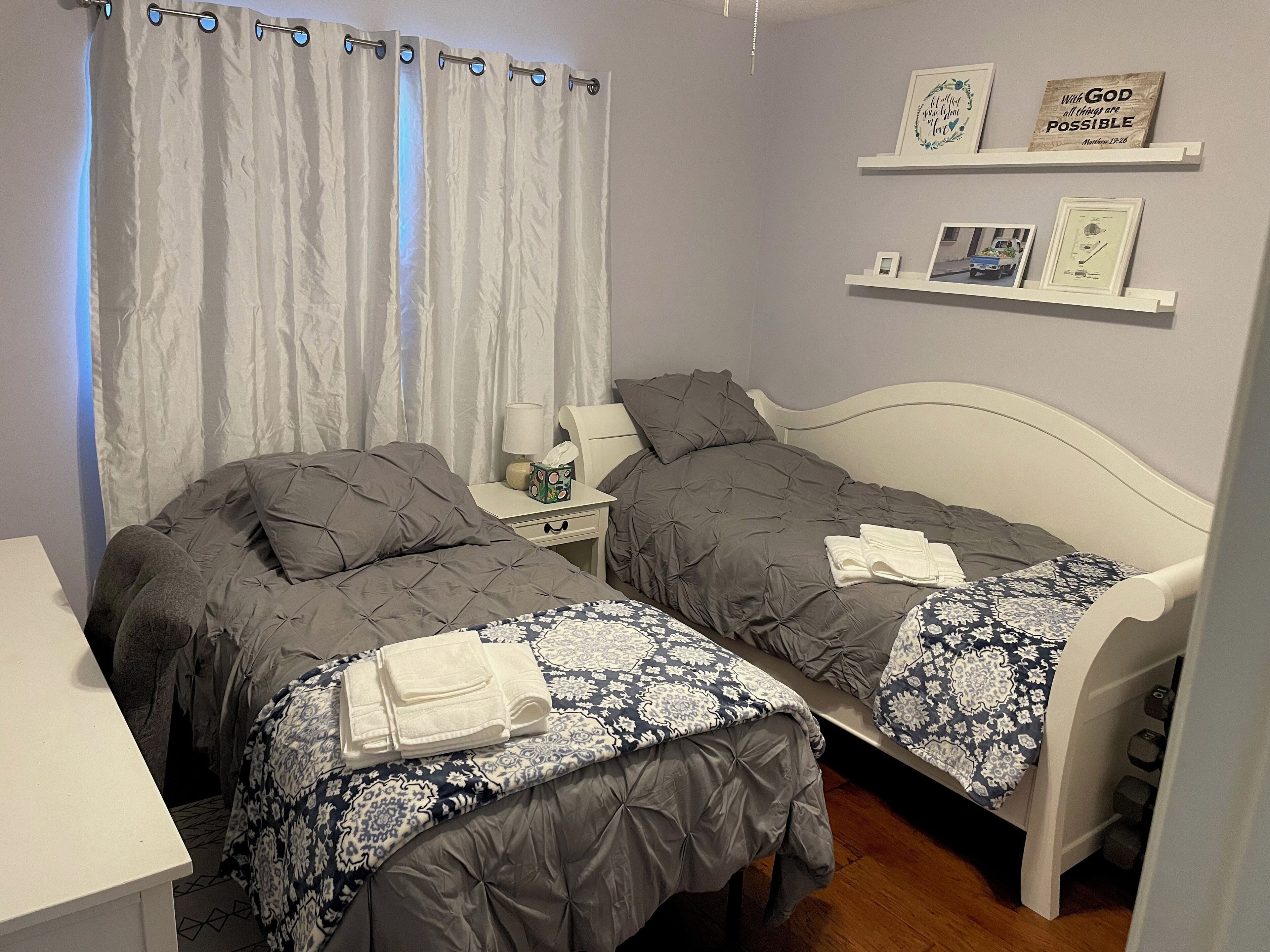 A bedroom with two beds, a nightstand, a lamp, and a shelf with framed pictures and a motivational quote.