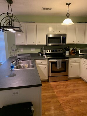 A kitchen with white cabinets, stainless steel appliances, a granite countertop, and a wooden floor. - Walking Distance to Masters, 3 Parking Spots, 3/2 with comforts of home (Augusta)