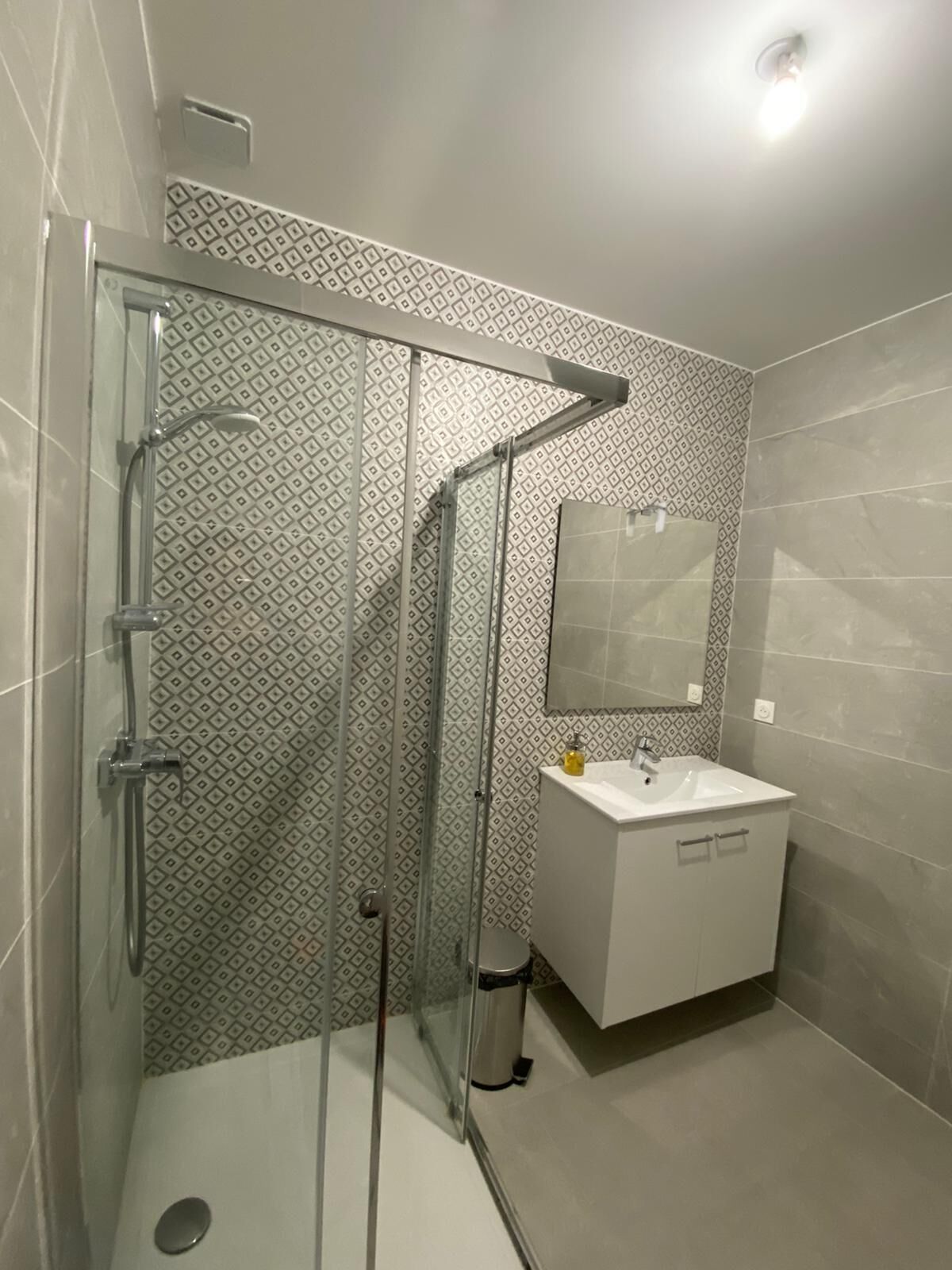 A modern bathroom with a glass shower enclosure, a white sink, and a mirror above it.