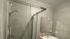 A modern bathroom with a glass shower enclosure, a white sink, and a mirror above it.