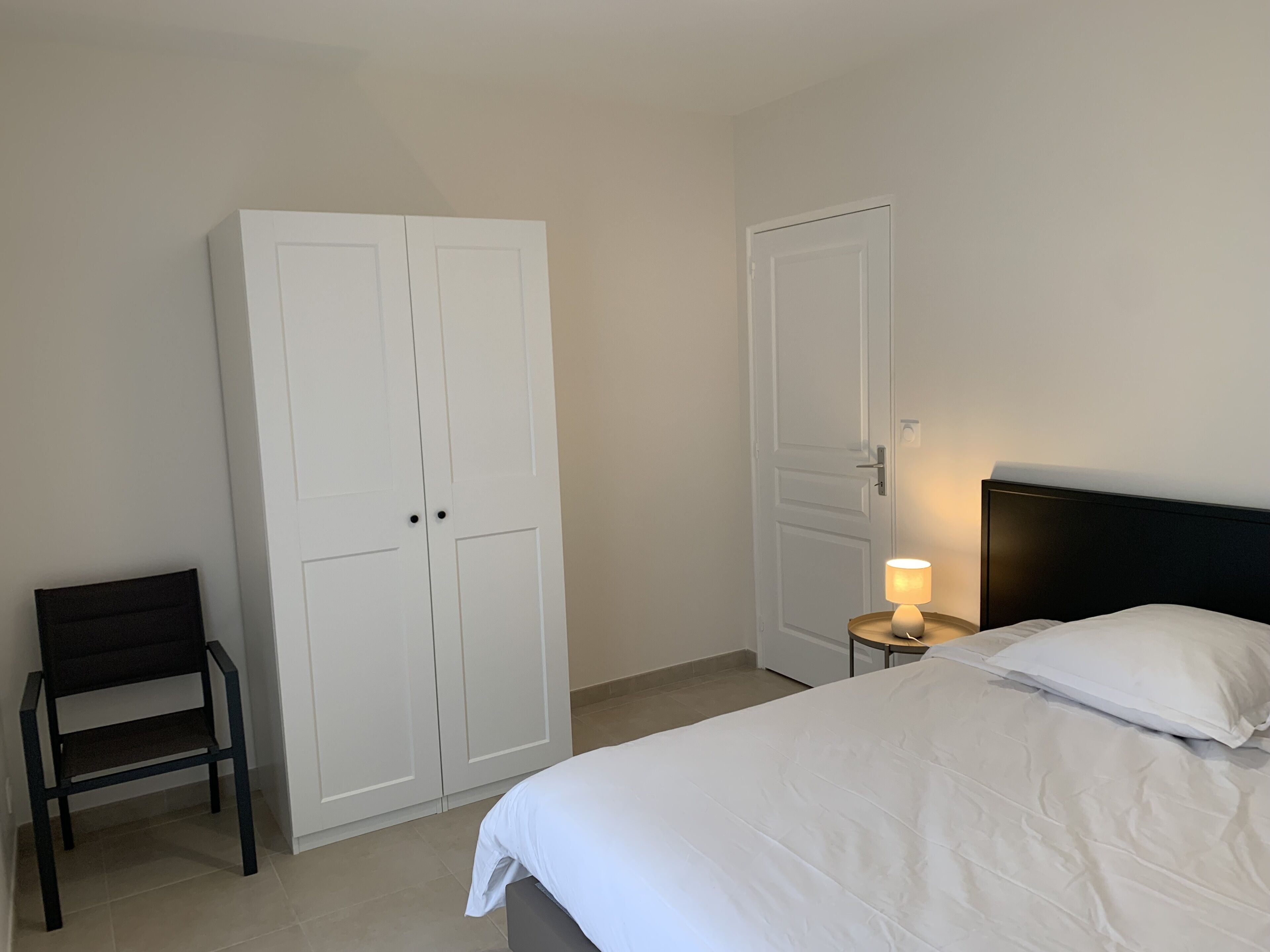 Ein Schlafzimmer mit Bett, Stuhl, Kleiderschrank und Nachttisch mit Lampe.