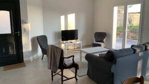 A modern living room with a sofa, armchairs, a TV, and a sliding glass door leading to an outdoor area.