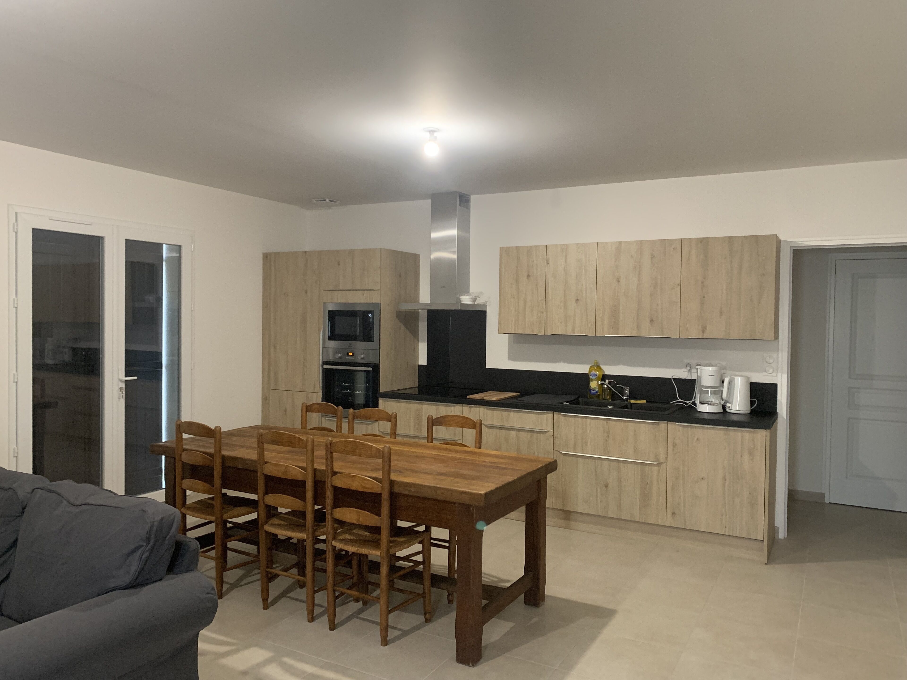 A modern kitchen with wooden cabinets, a dining table with chairs, and a coffee maker.
