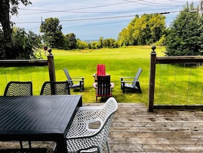A deck with outdoor seating, a view of a grassy area, and a red chair in the center. - The Blue House in the heart of Picton (Prince Edward)